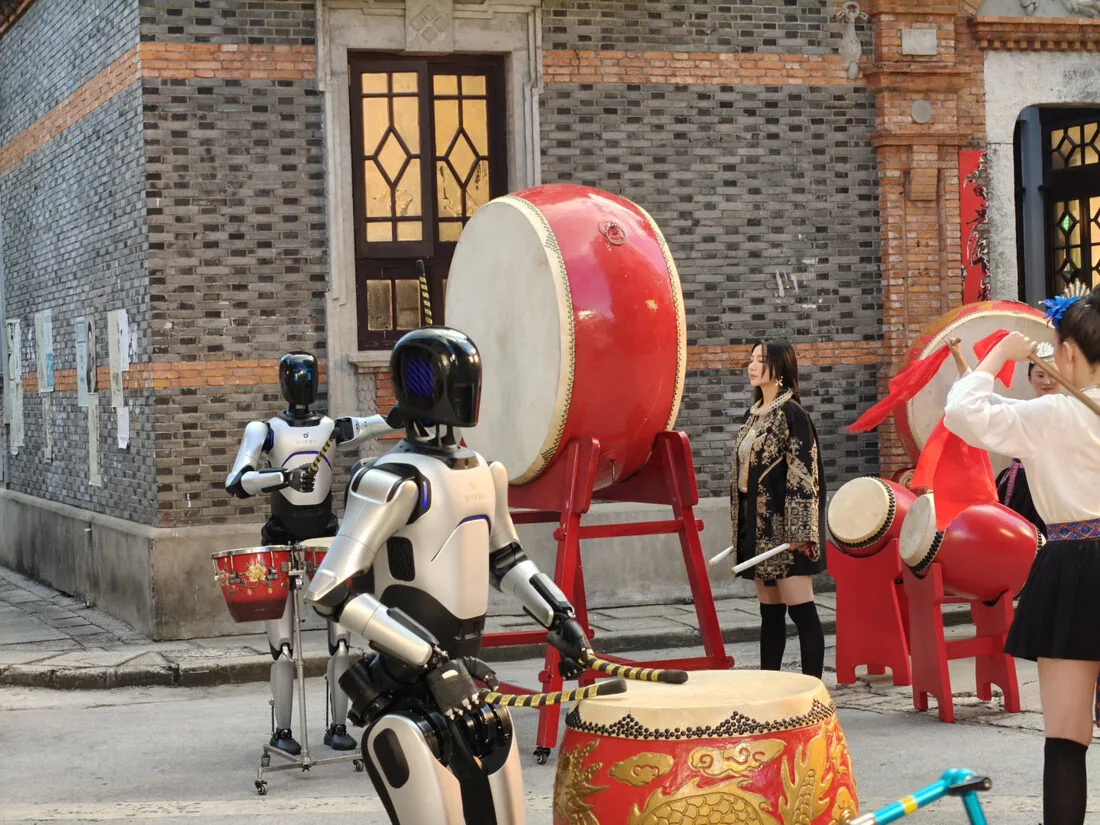 Two A2 Ultra robots performing a traditional drum show on a city street